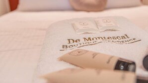 A bed with a white bedspread and a towel with 'De Montescal Boutique' branding.