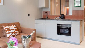 A compact kitchen with a built-in oven, a dining area with a brown sofa and a small table, and a large window above the sink.