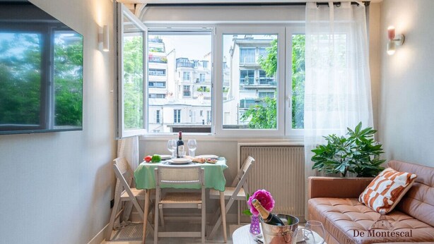 A cozy living room with a green table set for dining, a leather sofa, and a view of buildings through large windows.