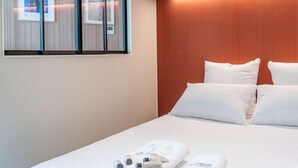 A hotel room with a bed, white pillows, a wooden headboard, and a wall-mounted TV. - De Montescal - Hot Tub A/C small appartment (Paris)