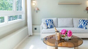 A modern living room with a sofa, a glass coffee table with a bottle and flowers, and a window with curtains. - De Montescal - Hot Tub A/C small appartment (Paris)