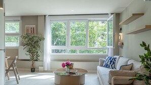 A modern living room with a large window, a round coffee table, a sofa, and a potted plant. - De Montescal - Hot Tub A/C small appartment (Paris)