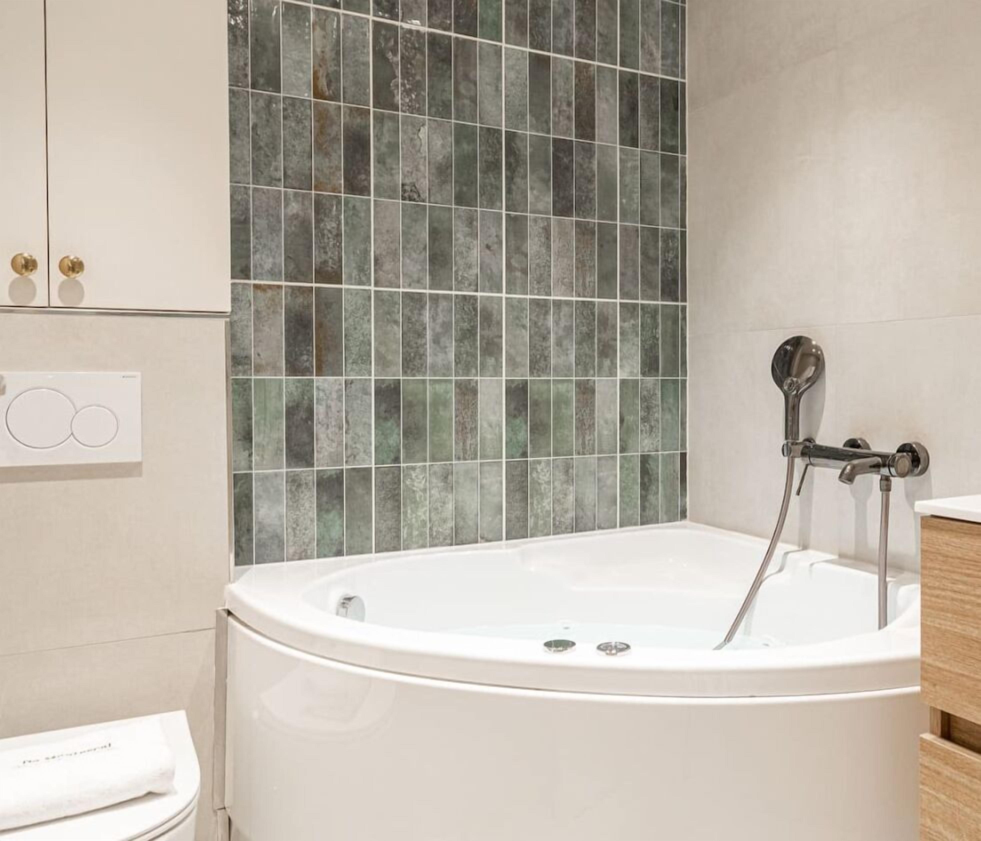 A modern bathroom with a freestanding bathtub, a shower with a handheld showerhead, and a tiled wall.
