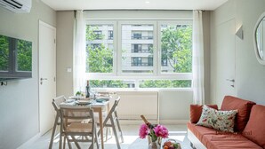 A modern apartment with a dining area, a sofa, and a large window with a view of buildings and trees. - De Montescal - Hot Tub A/C Wonder (Paris)