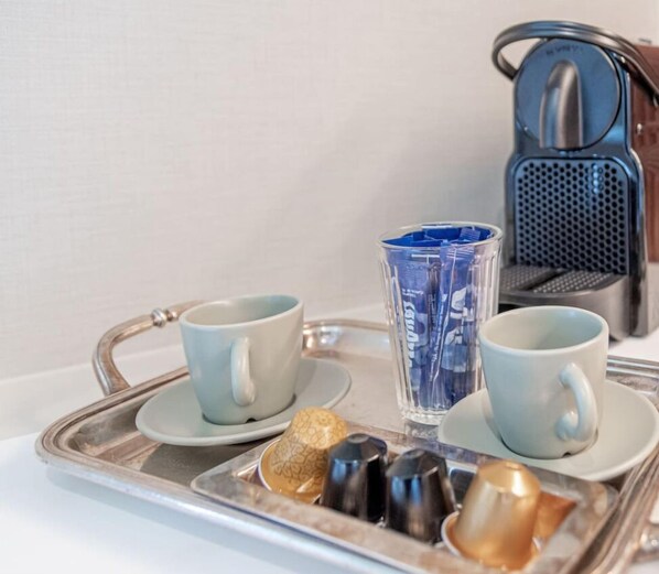 Uma bandeja com duas xícaras azul claro, um copo transparente com líquido azul e uma cafeteira de prata.