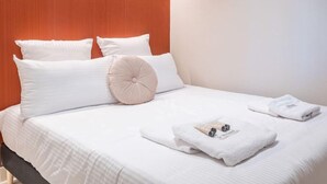 A neatly made bed with white linens, a wooden headboard, and a pair of towels on the side.