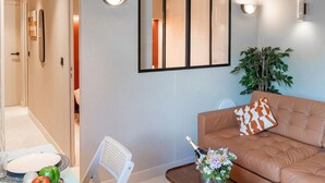 A modern living room with a brown sofa, a small table with a vase of flowers, and a wall-mounted mirror.