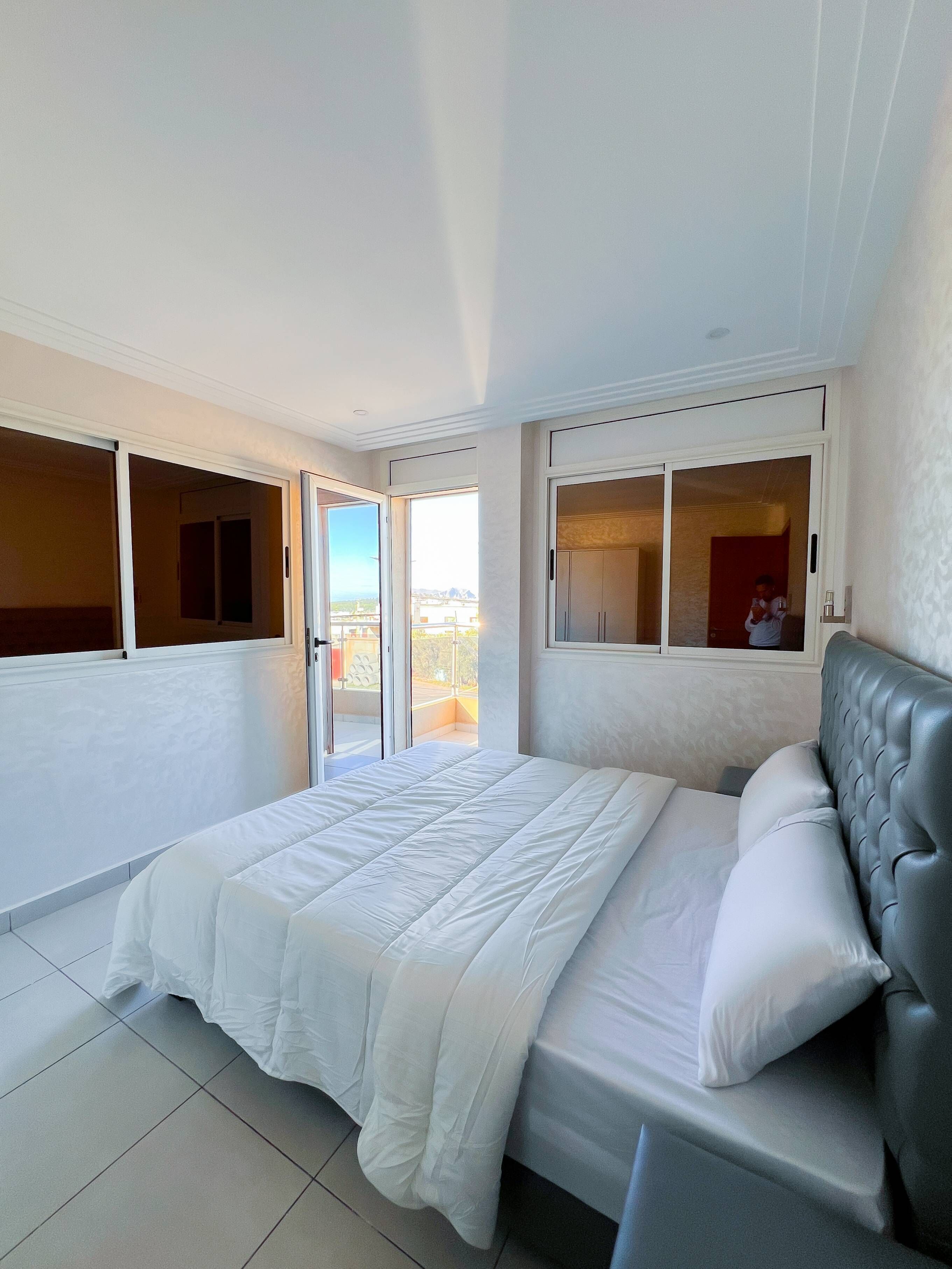 Une chambre à coucher avec un grand lit, une tête de lit rembourrée de couleur grise et une vue sur l’extérieur par une porte coulissante.