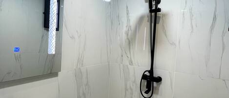 Un baño con lavamanos blanco, un espejo y una ducha con cabezal de ducha de mano.