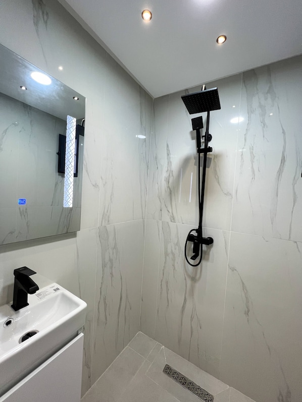 Une salle de bain avec un lavabo blanc, un miroir et une douche équipée d’un pommeau de douche amovible.