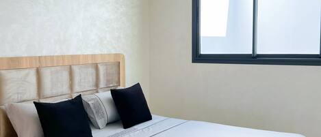 A modern bedroom with a wooden bed frame, a headboard with cushions, a large window, and recessed ceiling lighting.