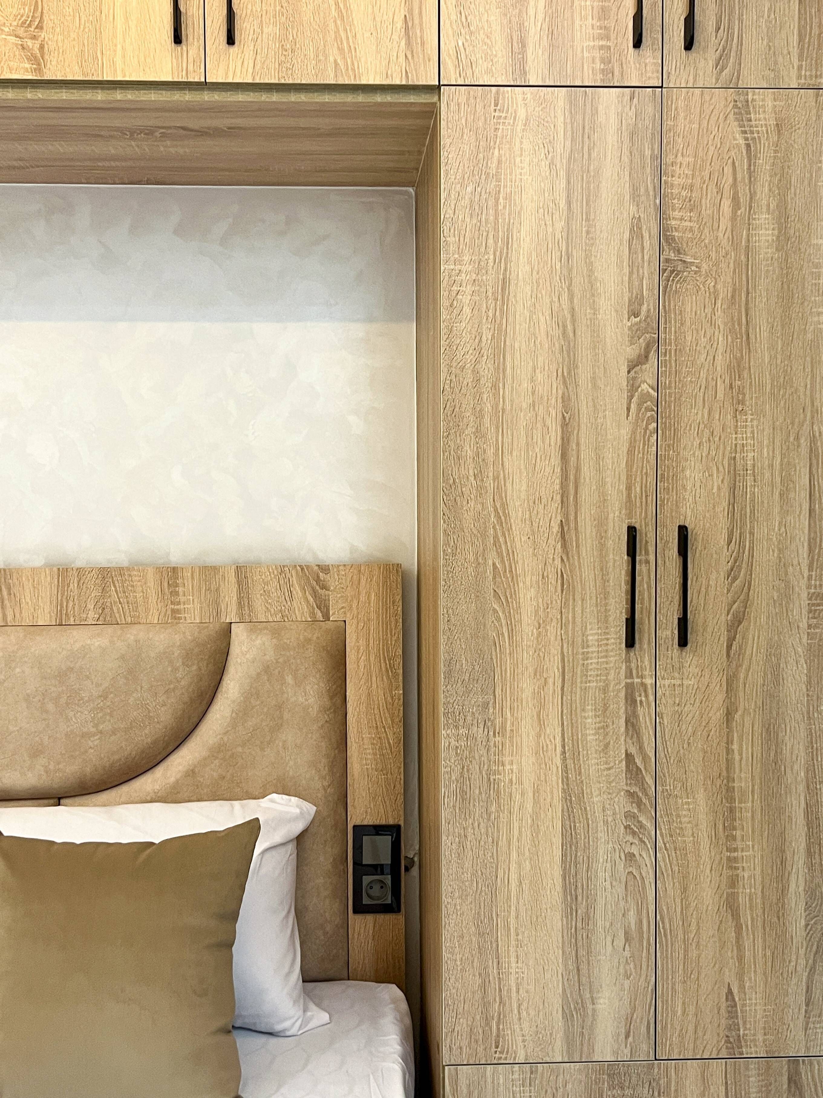 A bedroom with a bed, a wooden wardrobe, and a wall-mounted control panel.