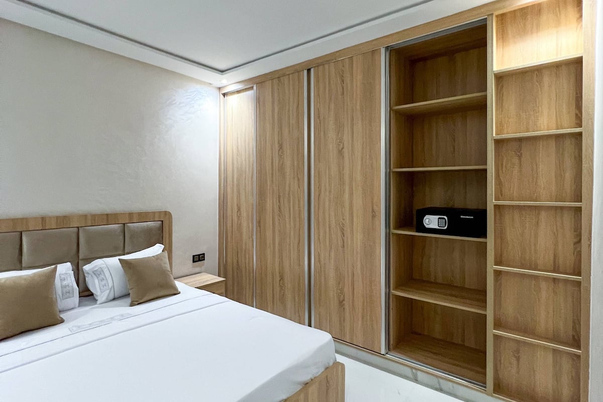 A modern bedroom with a large bed, wooden wardrobe, and built-in shelves.