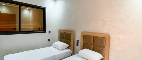 Una habitación de hotel con dos camas individuales, un ventanal grande y aire acondicionado integrado.