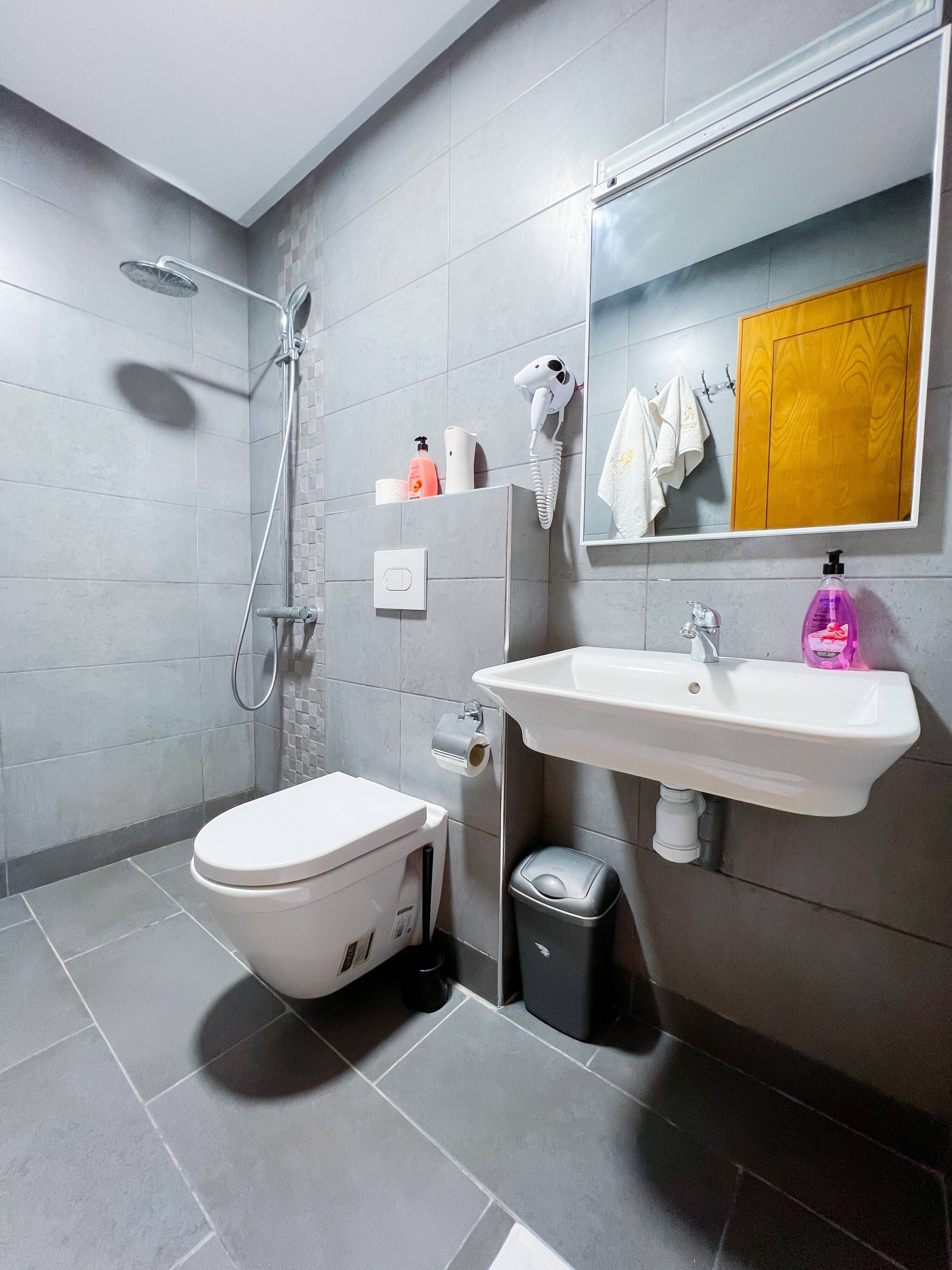 A modern bathroom with a toilet, sink, and shower. There is a mirror above the sink, and a towel rack with towels.