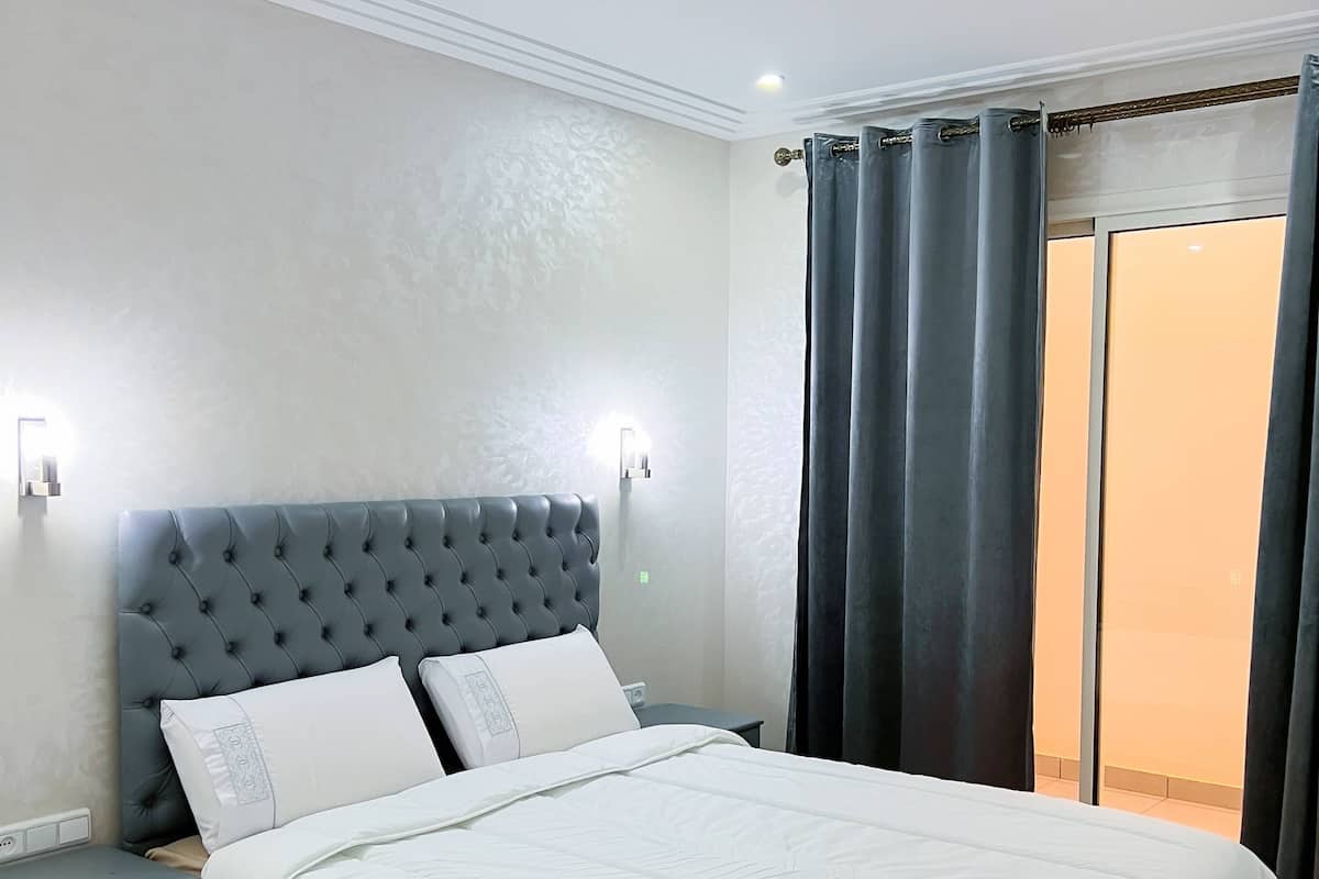 A bedroom with a tufted headboard, a bed with white bedding, a nightstand, and a wall-mounted light.