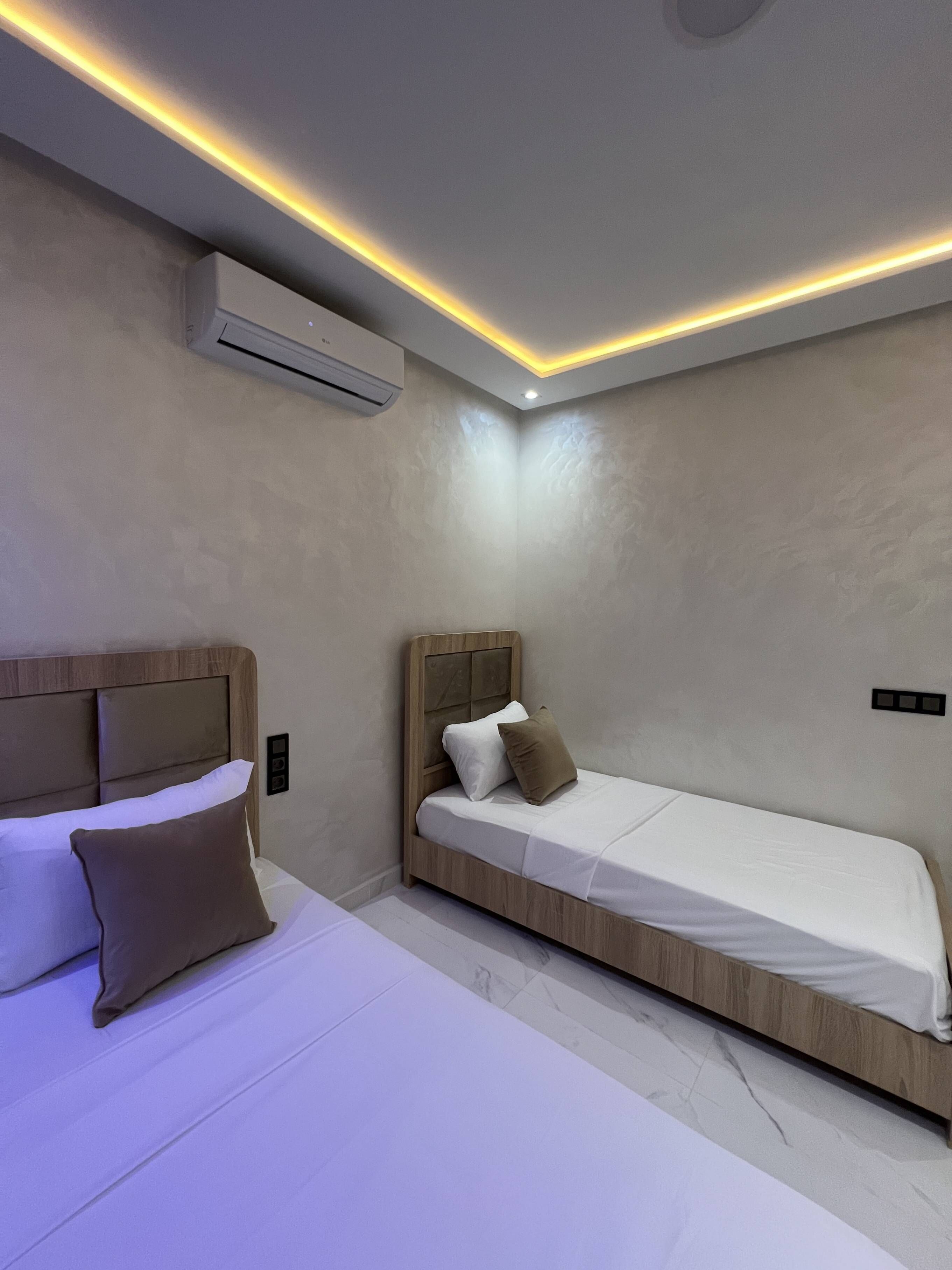 A modern bedroom with two beds, a ceiling light, and an air conditioning unit.