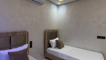 A modern bedroom with two beds, a ceiling light, and an air conditioning unit.