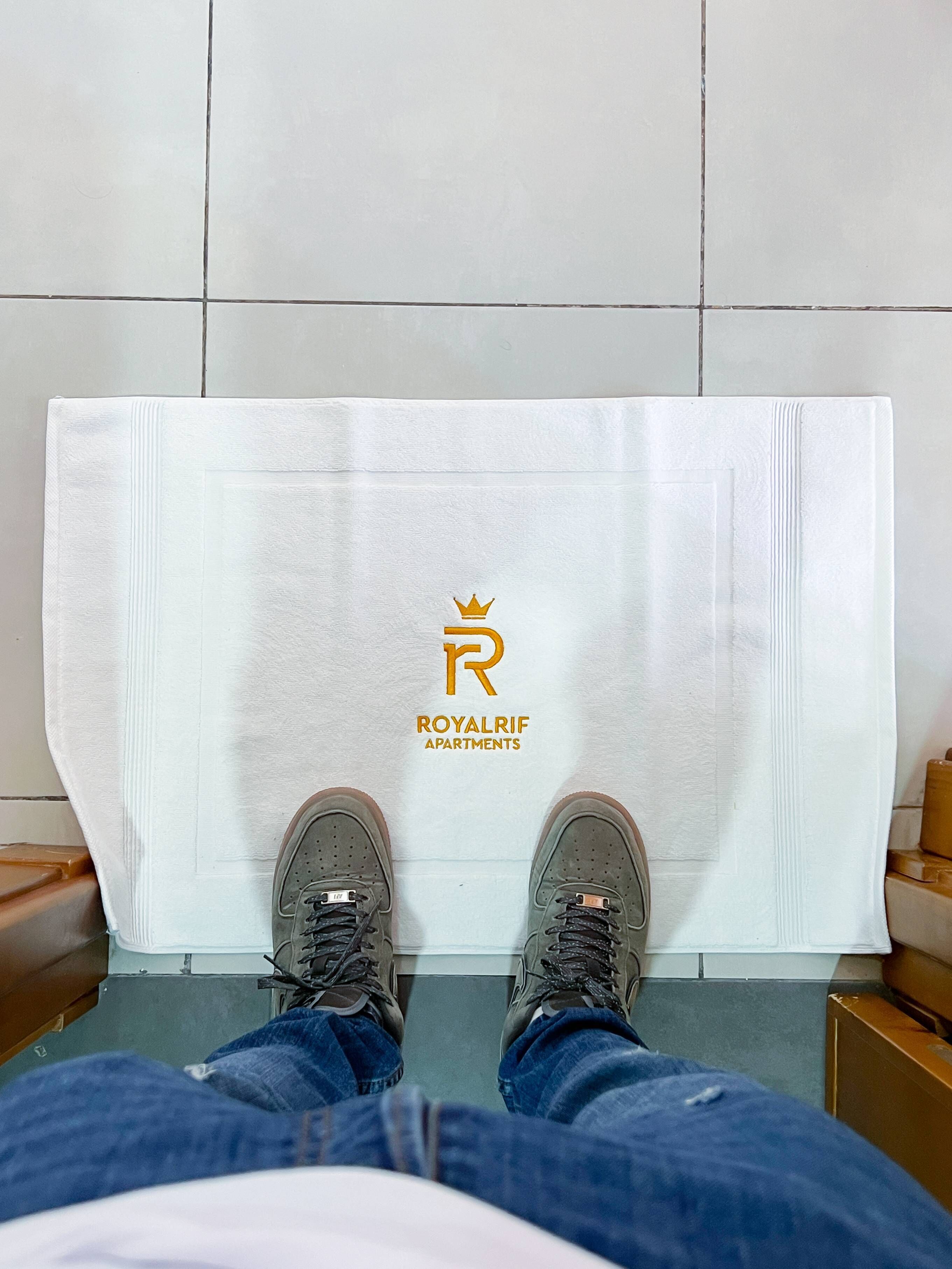 A person sitting with their feet on a white towel with the logo and name "ROYALRIF APARTMENTS" on it.