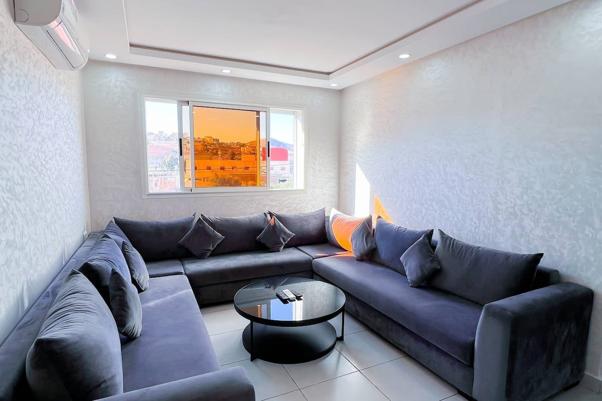 A modern living room with a sectional sofa, a glass coffee table, and a large window with a view of the cityscape.
