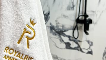 Una toalla blanca con texto bordado y un logotipo, colgada sobre una pared de mármol.