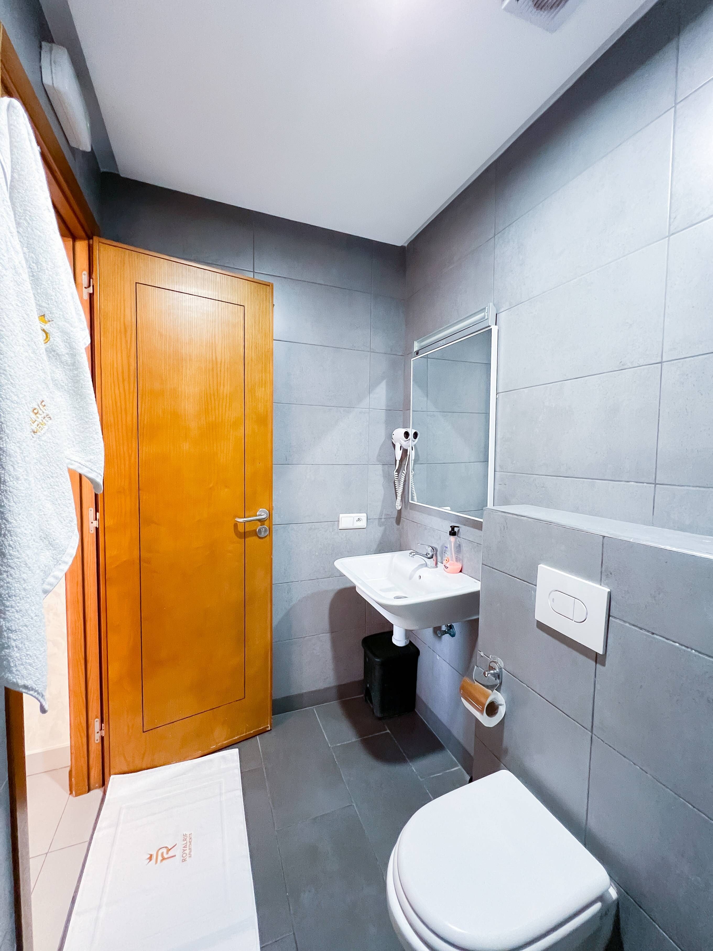 Un baño con puerta de madera, lavamanos blanco, espejo y retrete.