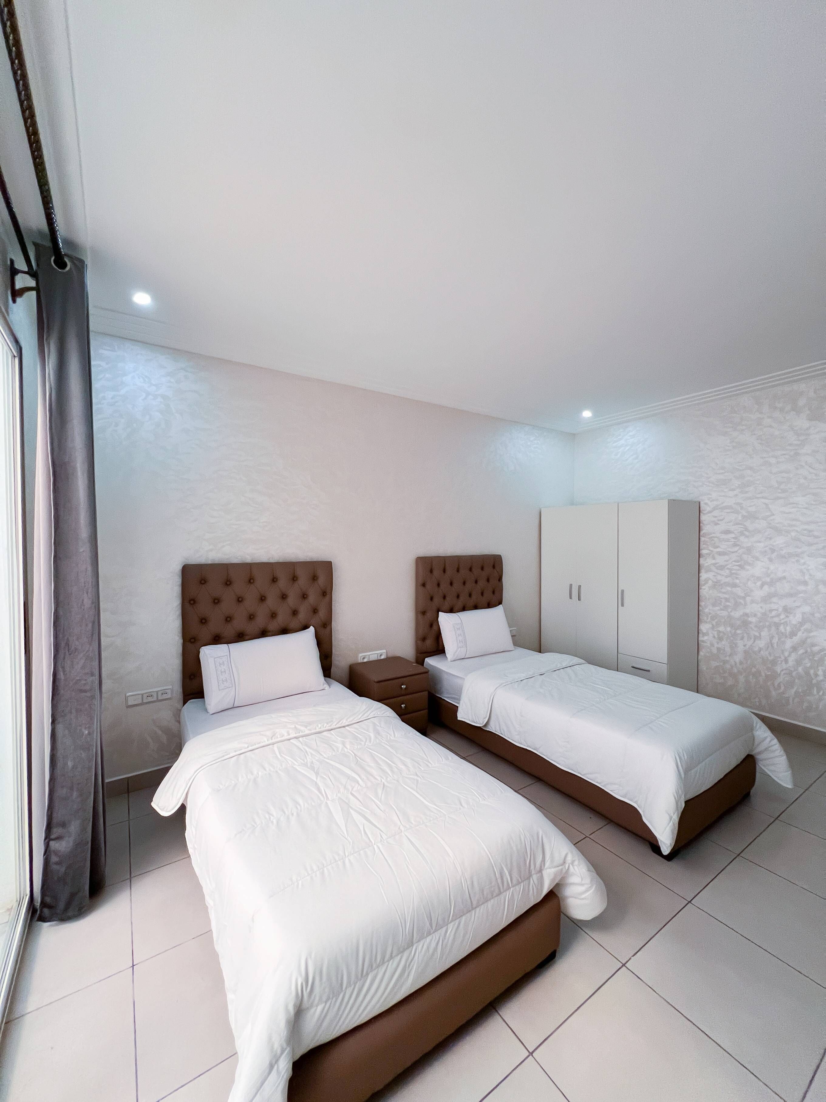 A bedroom with two beds, a wardrobe, and a window with curtains.