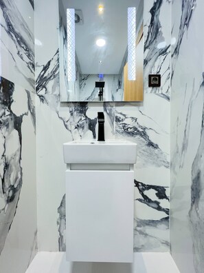 Une salle de bain avec un mur décoré de motifs en marbre, un lavabo blanc et un miroir au-dessus.