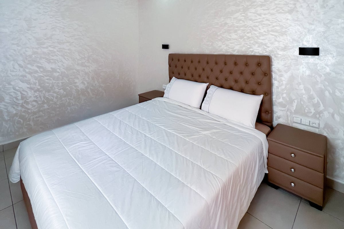 A modern bedroom with a large bed, a headboard, two bedside tables, and a patterned wall.