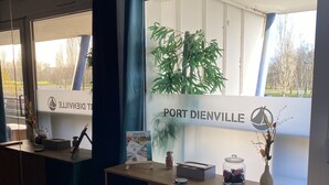 Ein Empfangsschalter mit Spiegel, Pflanze, einem Glasgefäß mit Dekoration und einem Schild mit der Aufschrift 'PORT DIENVILLE'.