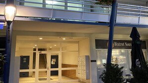 Ein Hotel Eingang mit Glastür, einer Treppe zu einer oberen Ebene sowie ein Schild für das Restaurant 'Bistrot Nouveau', das durch das Fenster sichtbar ist.