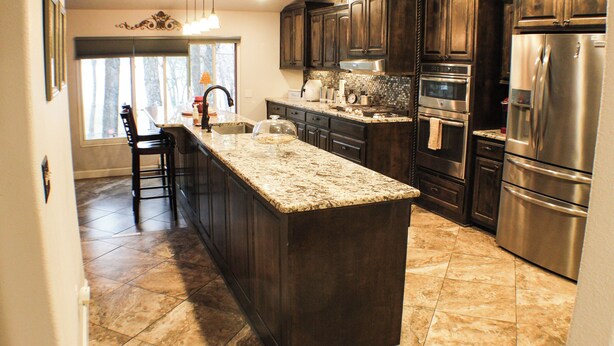 A kitchen with dark wood cabinets, stainless steel appliances, and a large granite island. - The Flathead Cottage: Family-Friendly Lake Fort Gibson Retreat (Hulbert)