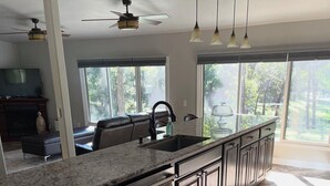 A spacious kitchen with a large island, dark cabinetry, and a view of the outdoors through large windows. - The Flathead Cottage: Family-Friendly Lake Fort Gibson Retreat (Hulbert)