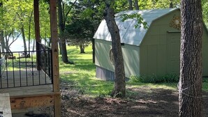 A covered outdoor area with a wooden deck, a metal gate, and a green shed with a metal roof. - The Flathead Cottage: Family-Friendly Lake Fort Gibson Retreat (Hulbert)