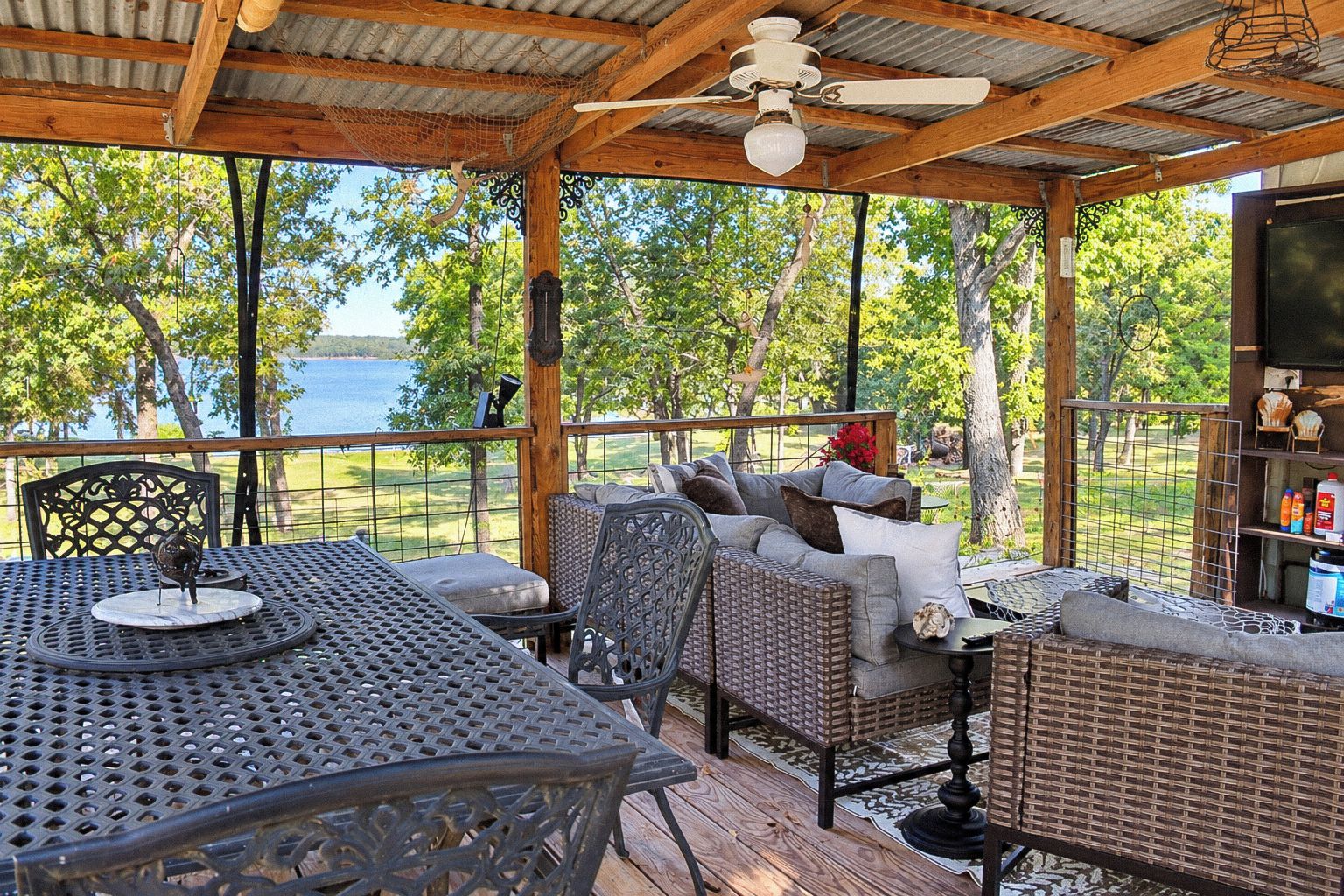 A covered outdoor seating area with a table and chairs, overlooking a body of water.
