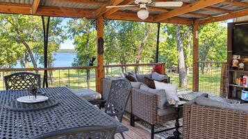 A covered outdoor seating area with a table and chairs, overlooking a body of water.