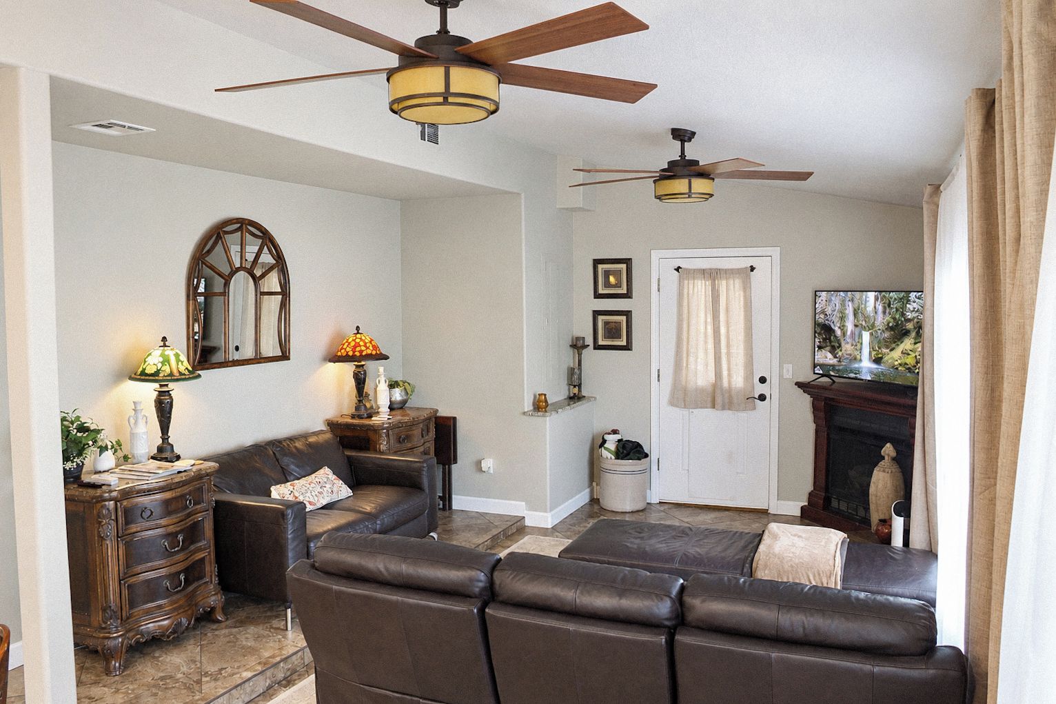 A living room with a sectional sofa, two ceiling fans, a television, and a fireplace.
