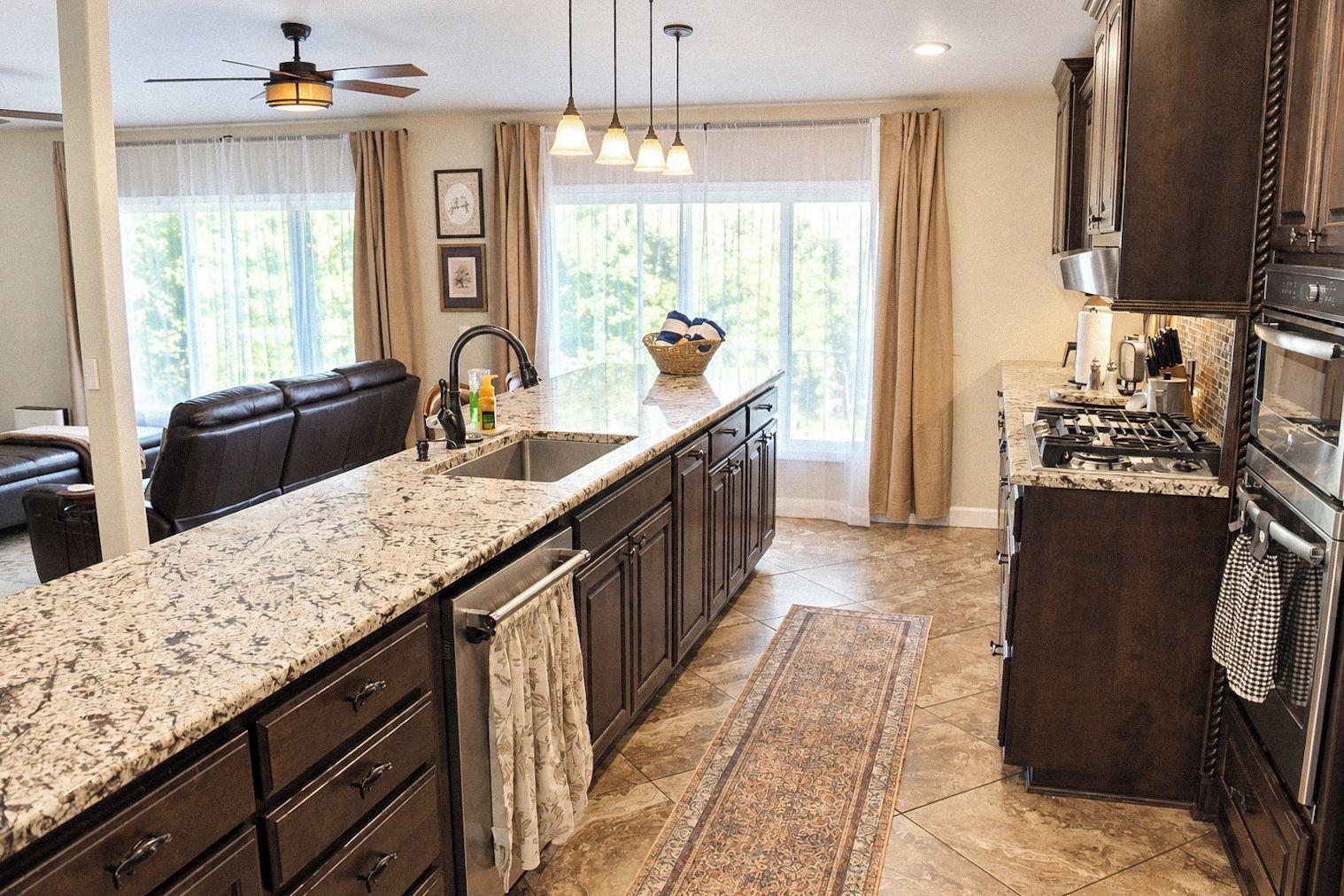 A kitchen with a granite countertop, dark cabinetry, a built-in oven, and a large window with curtains.