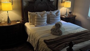 A neatly made bed with white linens and rolled towels, flanked by two bedside tables with lamps, in a room with a classic wooden headboard and tiled flooring. - The Flathead Cottage: Family-Friendly Lake Fort Gibson Retreat (Hulbert)
