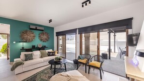A modern living room with a teal accent wall, a white sofa, a coffee table, and a seating area with chairs. - SunnyVillas: 3BR New Modern Villa*Private Pool*HVN (Paralimni)