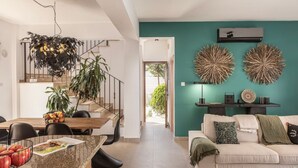 A modern living room with a teal accent wall, a dining area with a wooden table and chairs, and a staircase leading to an upper level. - SunnyVillas: 3BR New Modern Villa*Private Pool*HVN (Paralimni)