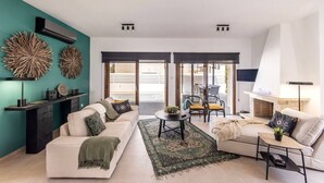 A modern living room with a sofa, coffee table, and a fireplace. There are decorative wall art pieces and a large window with blinds. - SunnyVillas: 3BR New Modern Villa*Private Pool*HVN (Paralimni)