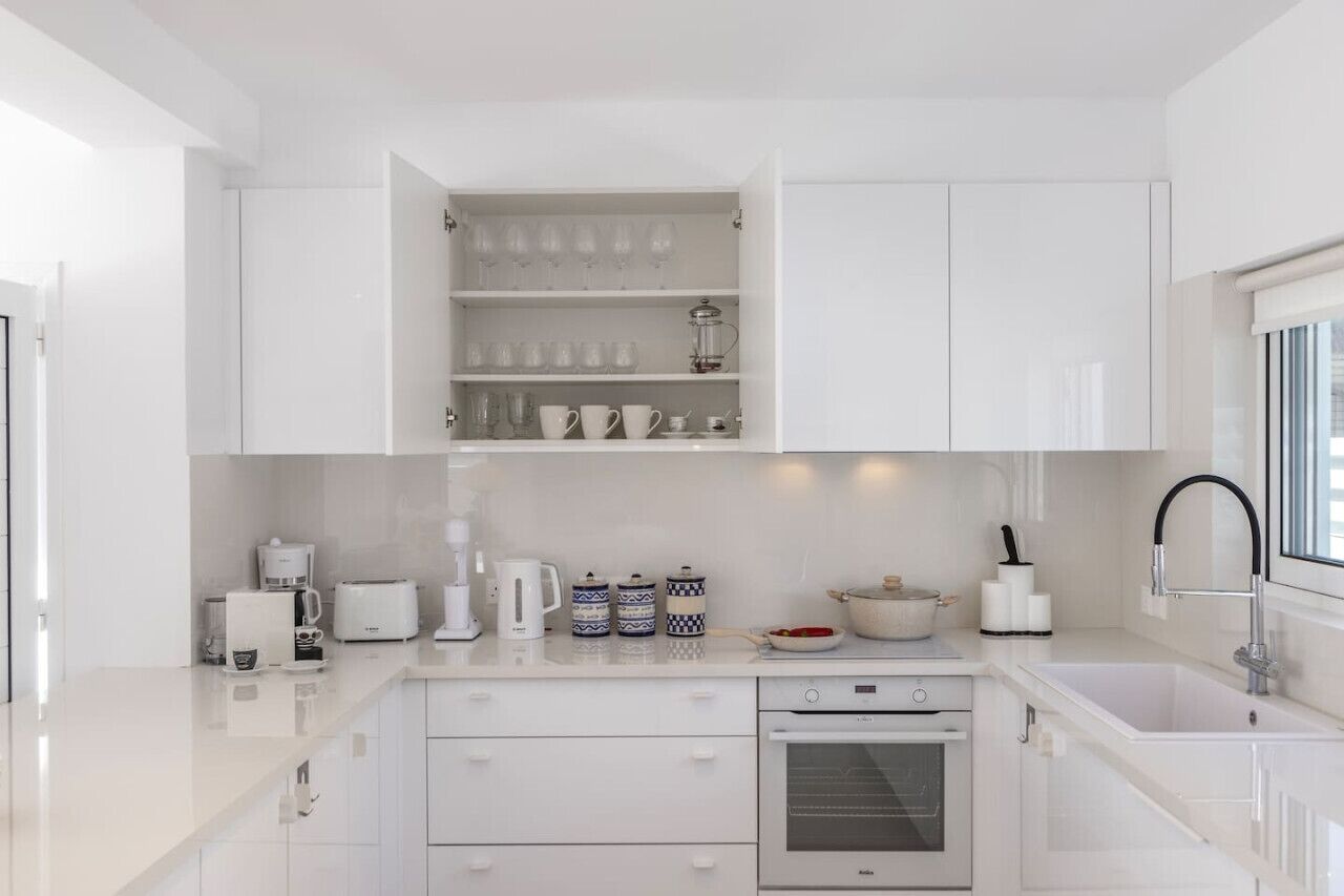 Une cuisine moderne avec des meubles blancs, un four encastré, un coin café et une fenêtre offrant une belle vue.