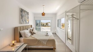A modern bedroom with a bed, bedside table, and a view of the outdoors. - SunnyVillas: 3BR New Modern Villa*Private Pool*BLG (Paralimni)