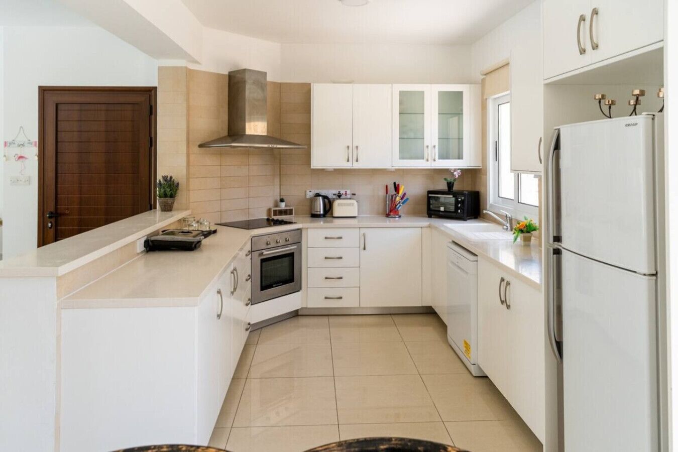 A modern kitchen with white cabinets, a stainless steel range hood, a built-in oven, a microwave, and a refrigerator.