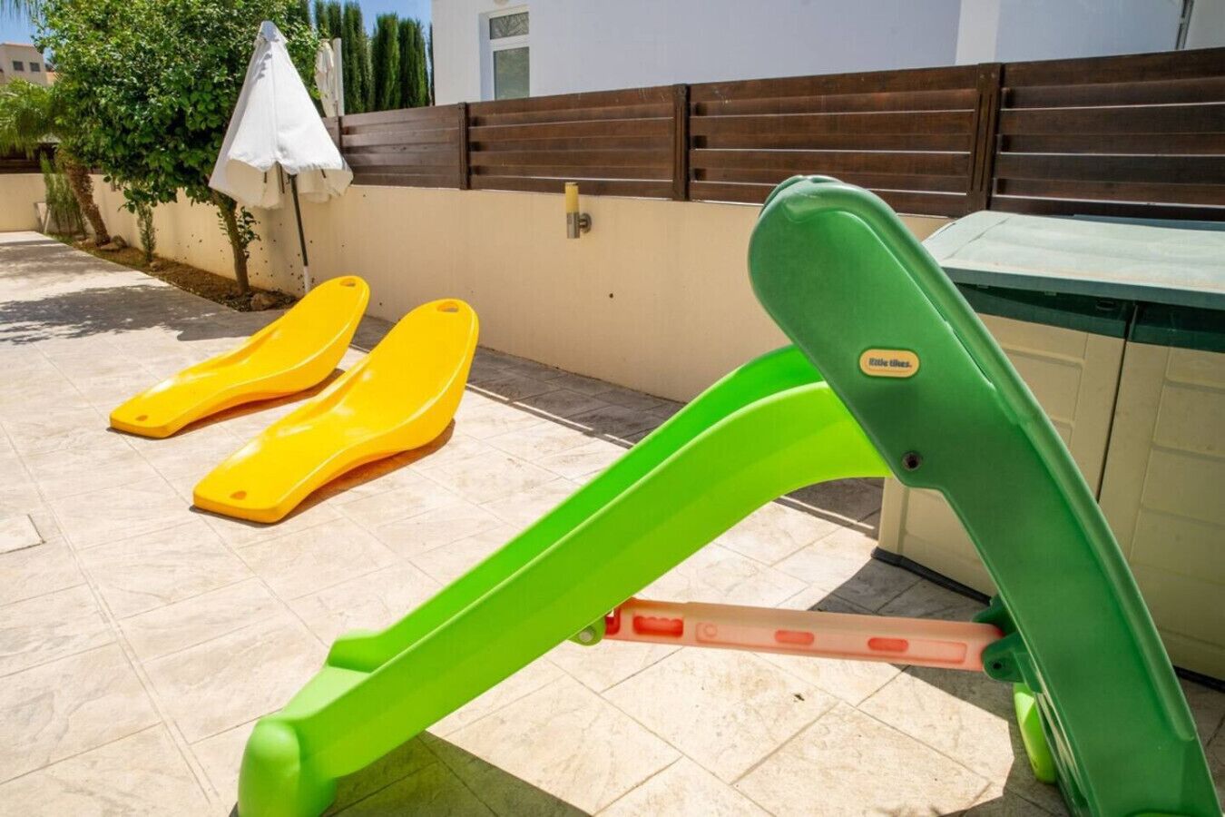 Eine Terrasse mit grünen Trainingsgeräten, gelben Rutschen und einem weißen Sonnenschirm.