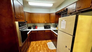 Una cocina compacta con armarios de madera, un refrigerador, un microondas y una estufa.