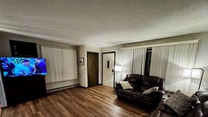 Una sala de estar con piso de madera, un sofá de cuero marrón, un televisor y una puerta.