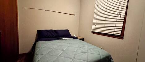 Un dormitorio con una cama, una ventana con persianas, una puerta de madera y un ventilador de techo.