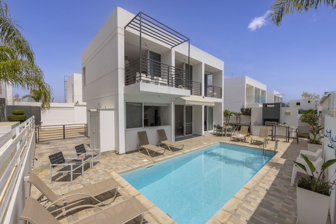 Una casa moderna de dos pisos con piscina, mobiliario exterior y un balcón.